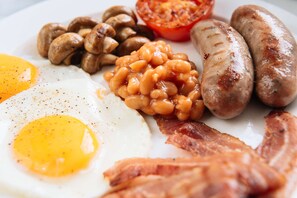 Un plato de desayuno con huevos, tocino, salchichas, champiñones y frijoles horneados.