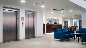 Eine moderne Lobby mit einer Rezeption, zwei Aufzügen und einer blauen Sitzgruppe.