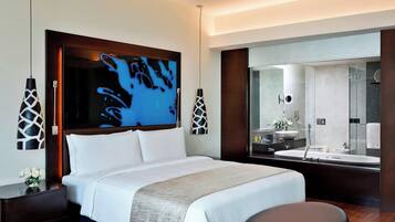 A modern hotel room with a large bed, a sitting area, a bathroom with a large mirror, and artwork on the wall.