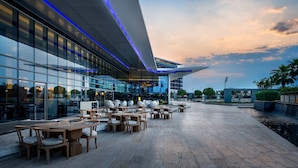 An outdoor seating area with tables and chairs, a modern building with glass windows, and a water feature. - Marriott Hotel Al Forsan, Abu Dhabi (Abu Dhabi)