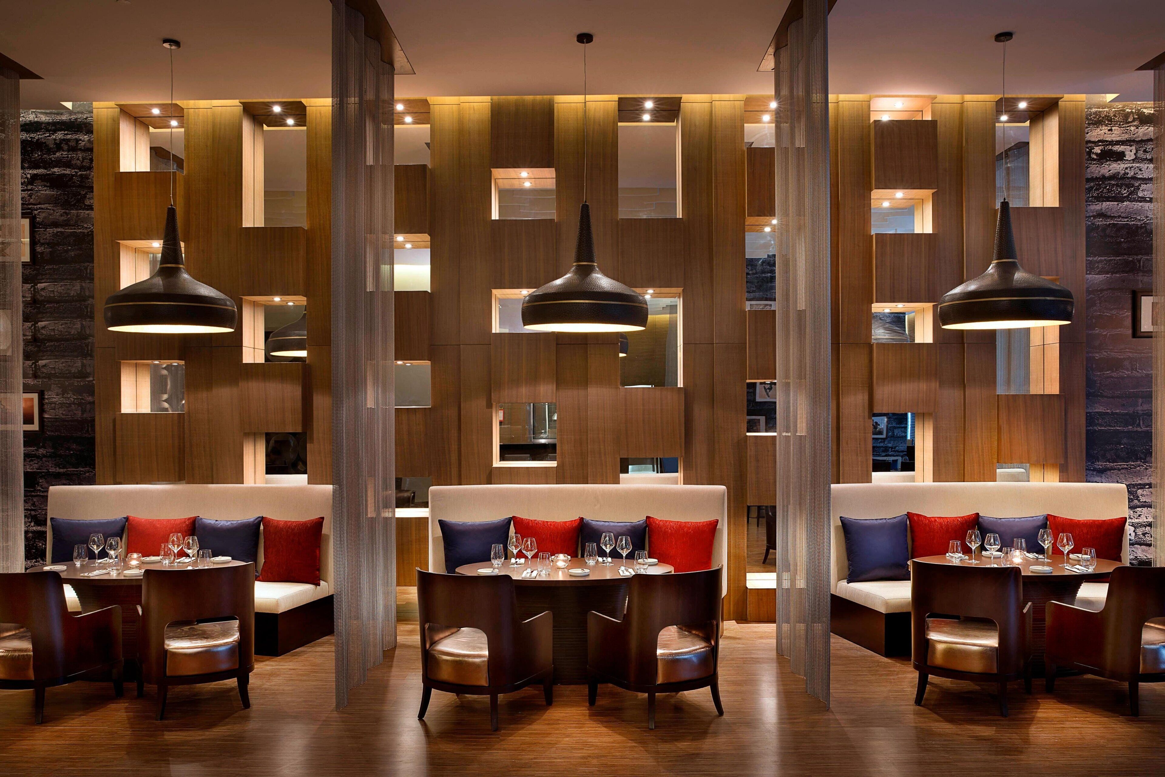 A modern dining area with wooden panel walls, pendant lighting, and a central seating area with tables and chairs.