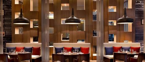 A modern dining area with wooden panel walls, pendant lighting, and a central seating area with tables and chairs.
