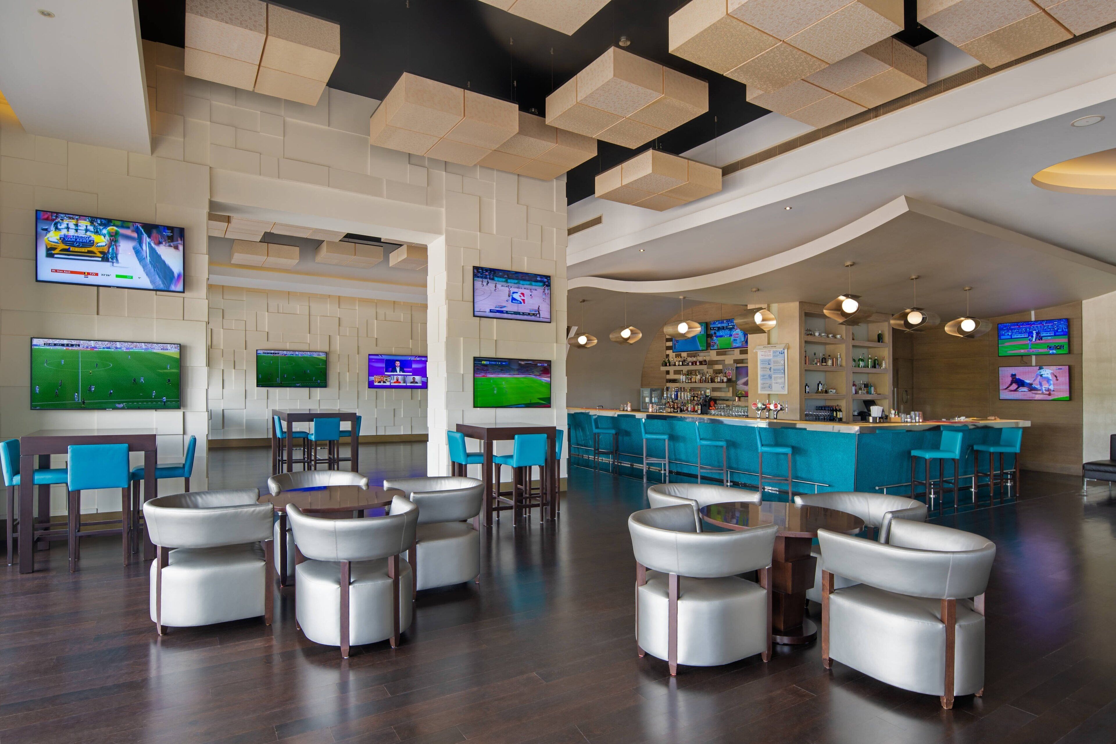 A modern bar area with multiple screens displaying sports events, bar stools, and a counter with a bartender.