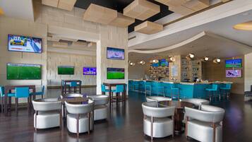A modern bar area with multiple screens displaying sports events, bar stools, and a counter with a bartender.