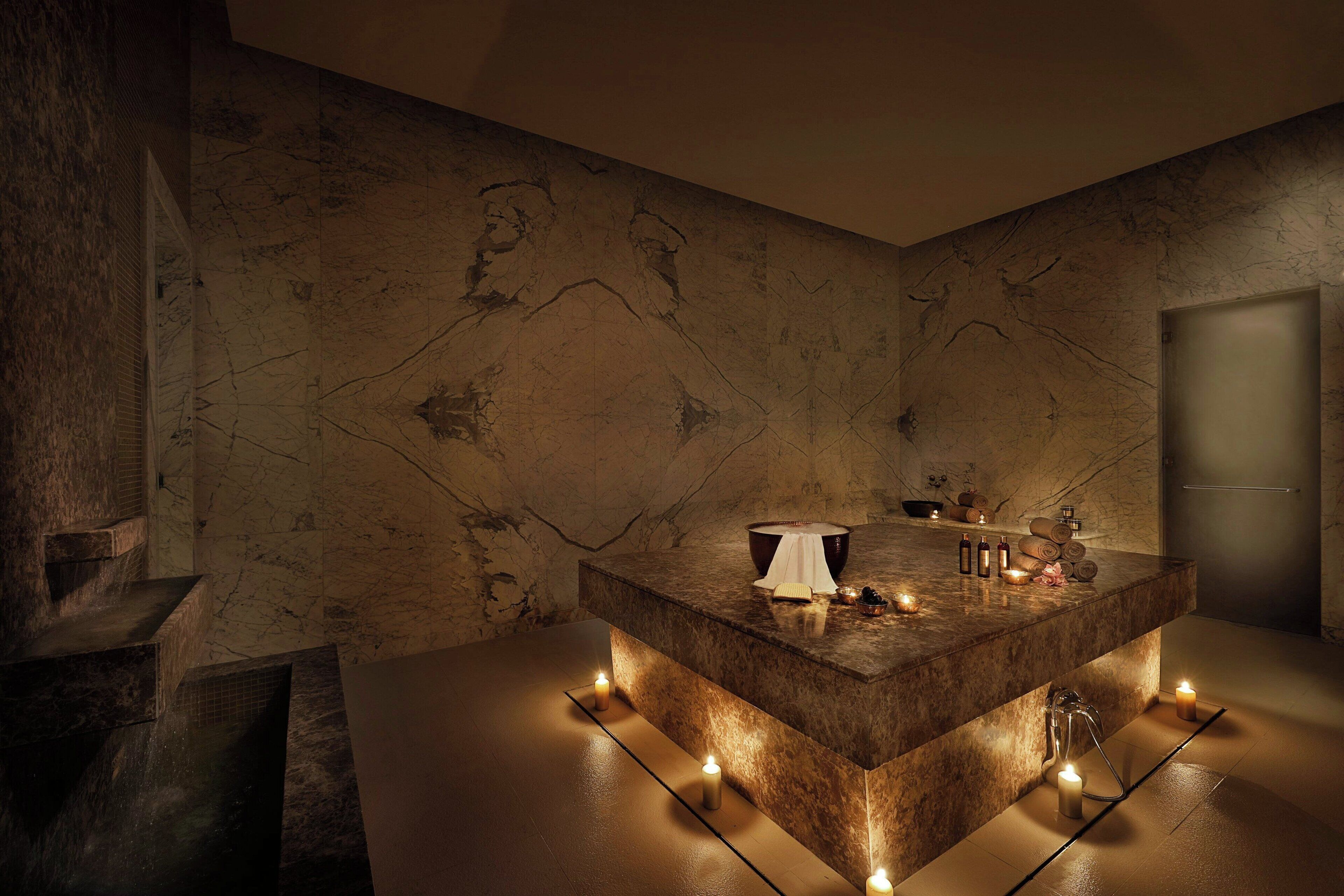 Une salle de bain moderne avec un comptoir en marbre, un lavabo et un miroir. On y trouve des bougies posées sur le sol et un porte-serviettes au-dessus du lavabo.