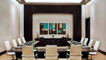 A conference room with a long table, white chairs, and a dark wooden backdrop.