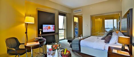 Habitación de hotel con cama, escritorio, silla, televisor y vistas al exterior.
