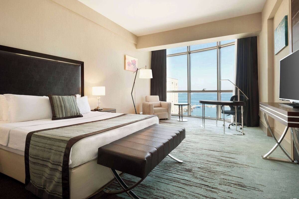 A hotel room with a large bed, a desk, a chair, and a view of the ocean.