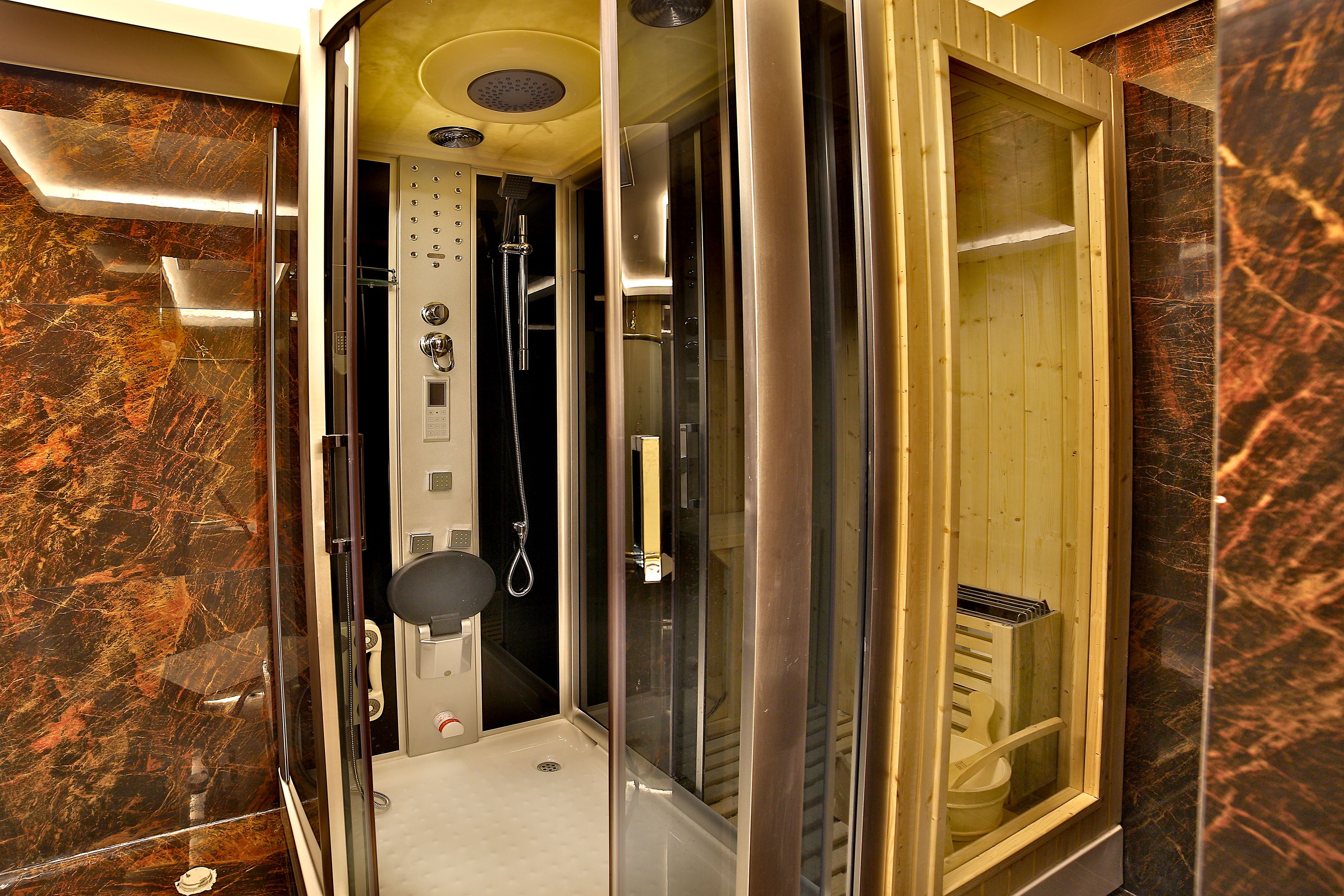 Un baño moderno con ducha envuelta en vidrio, paredes de mármol y tocador de madera.