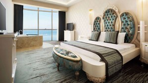 A spacious bedroom with a large bed, a vanity, a television, and a view of the sea. - Ramada by Wyndham Iskenderun (Iskenderun)