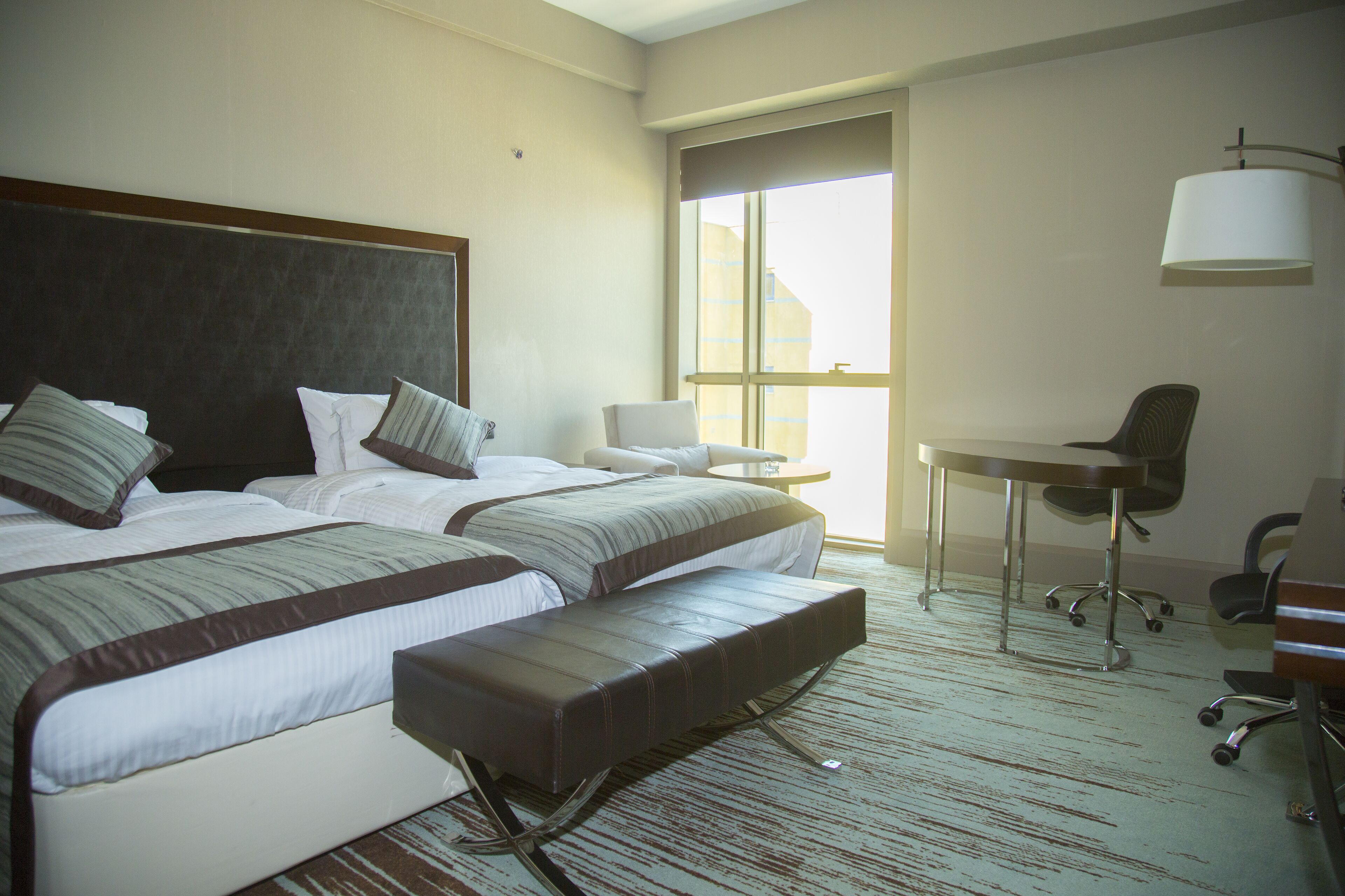 A hotel room with two beds, a desk, a chair, and a large window.