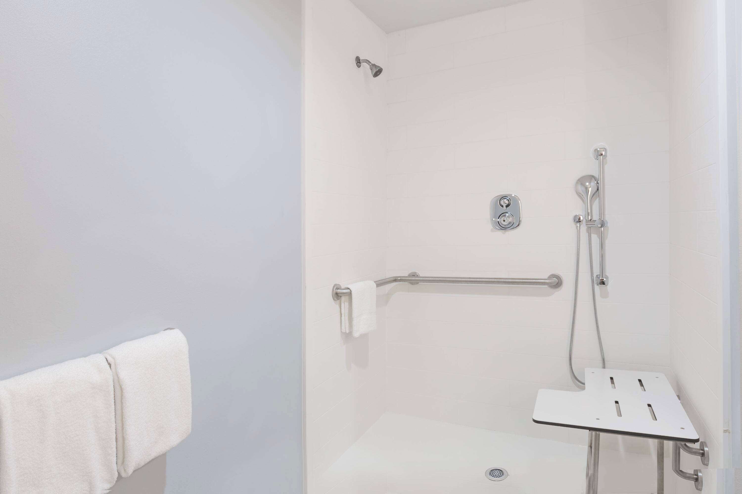 A shower with a grab bar, a towel rack, and a shower control panel.