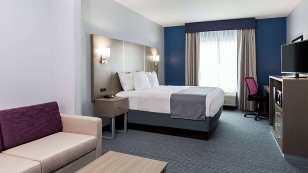 A hotel room with a bed, a desk, a chair, a TV, and a couch. - Days Inn & Suites by Wyndham Houston NW Cypress (Houston)