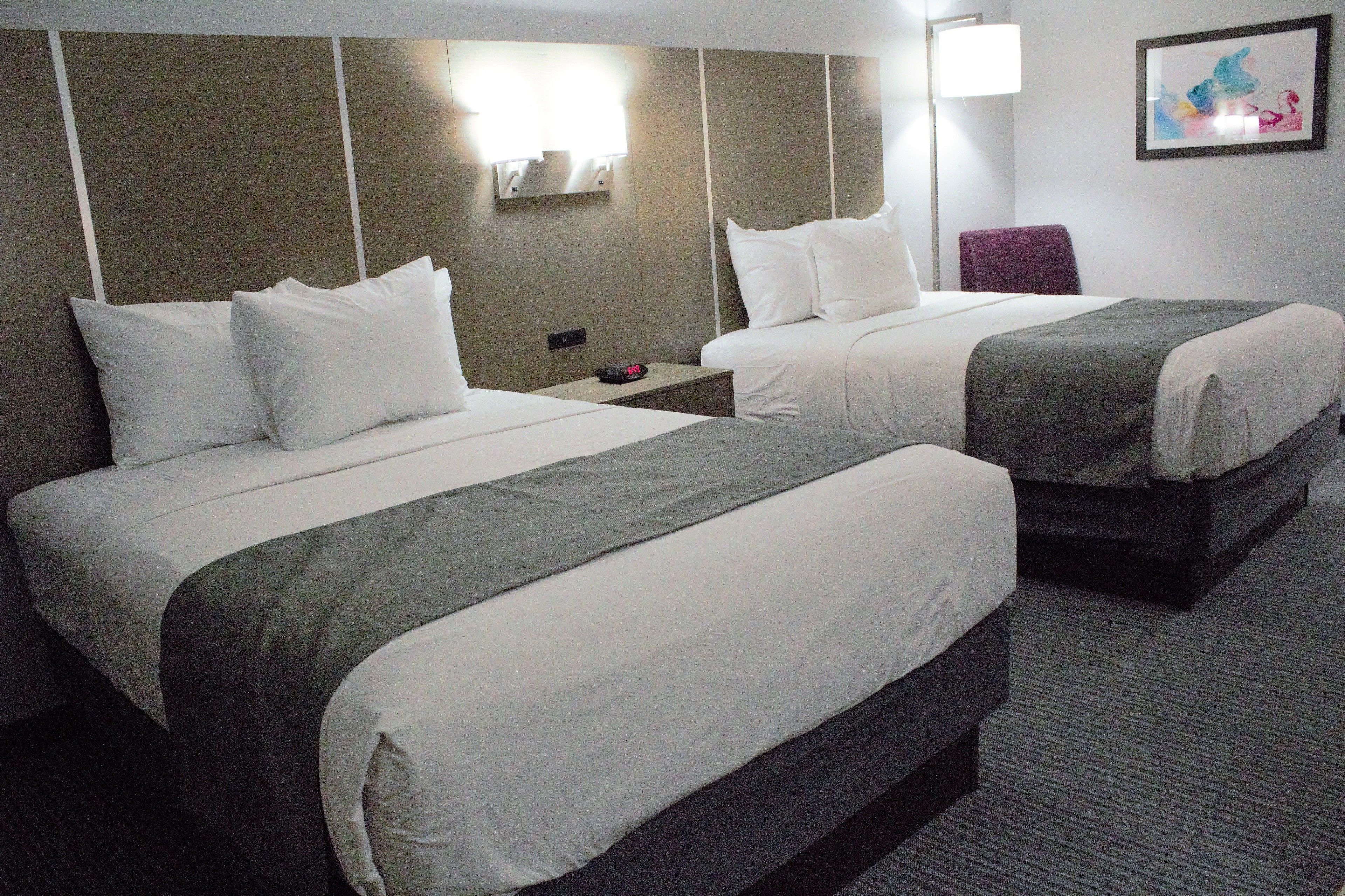 Habitación de hotel con dos camas, una mesita de noche, una lámpara y un cuadro en la pared.