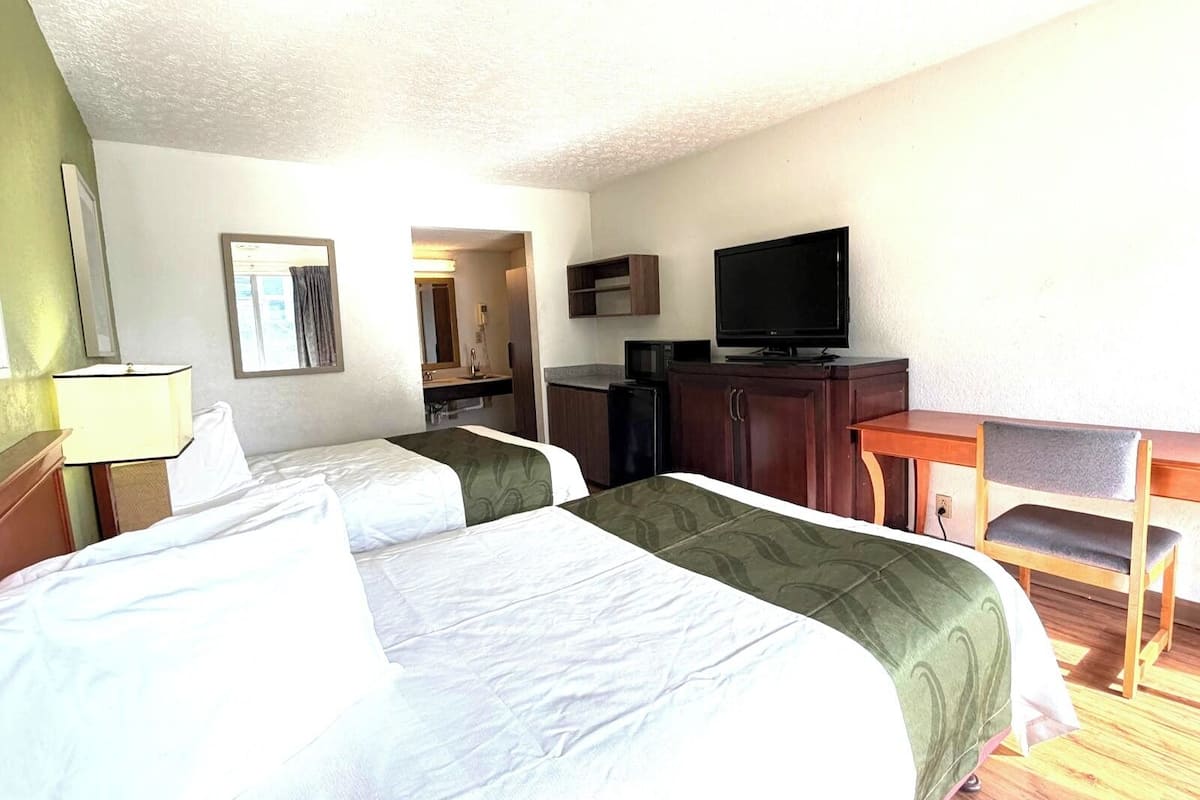A hotel room with two beds, a TV, a desk, and a mirror.