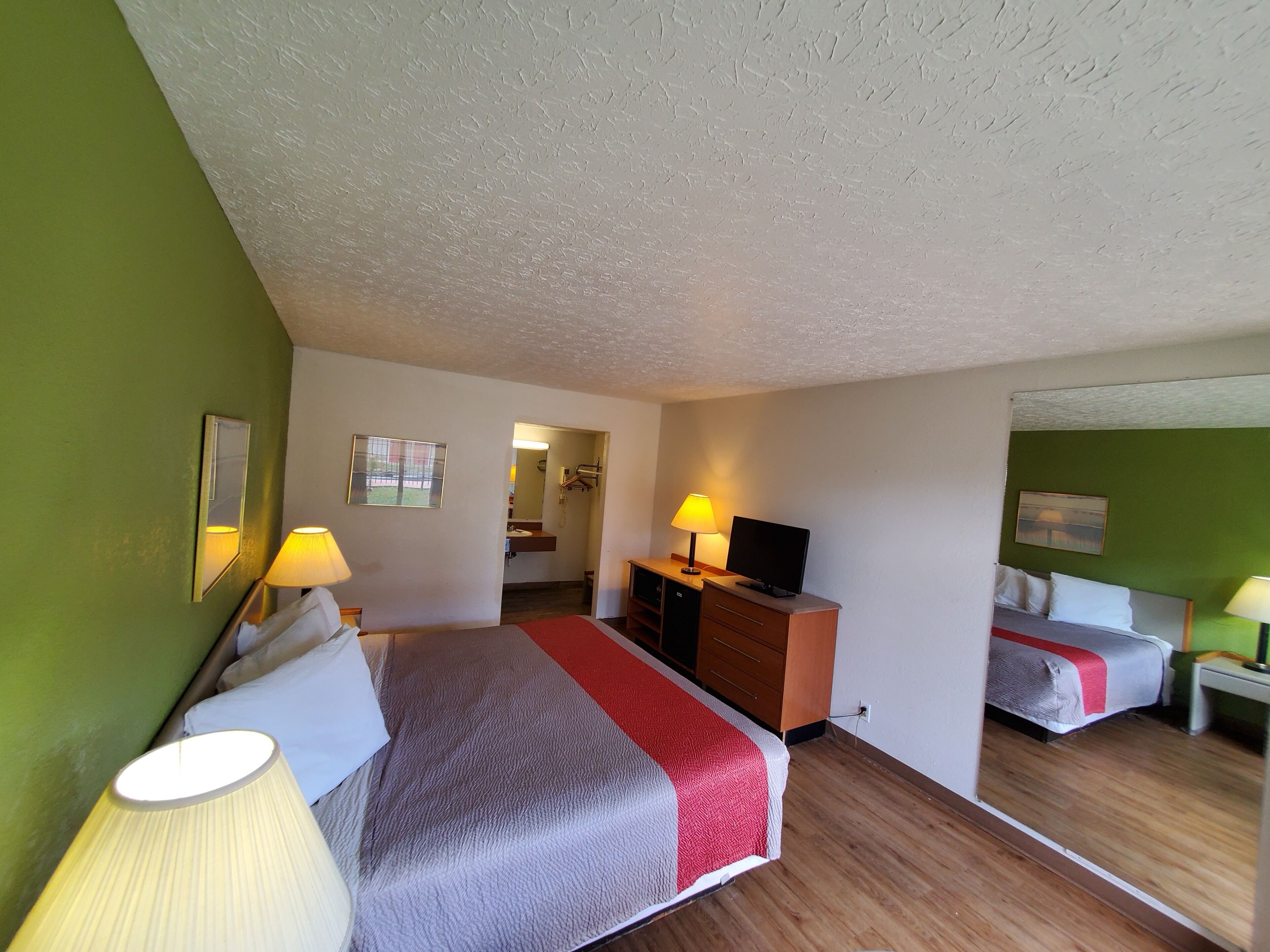 Een hotelkamer met een bed, bureau, stoel, televisie en spiegel.