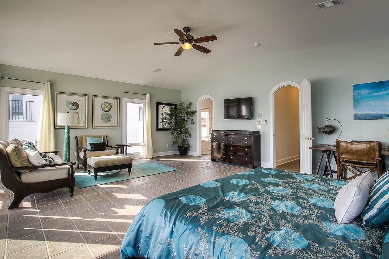 Une chambre spacieuse avec un grand lit, un ventilateur de plafond, une commode et un téléviseur.