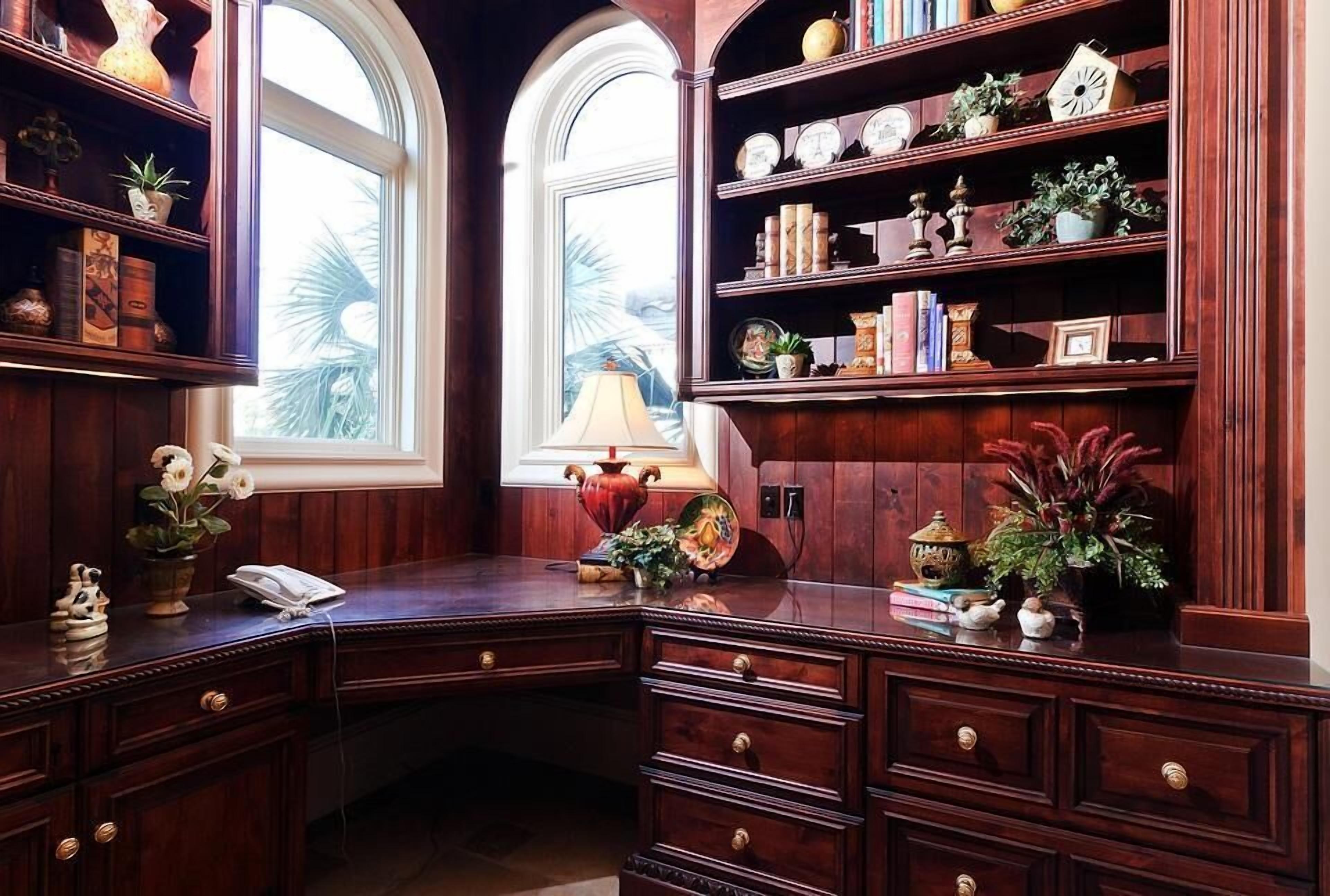 A study with a desk, bookshelves, and a window with a view of palm trees.