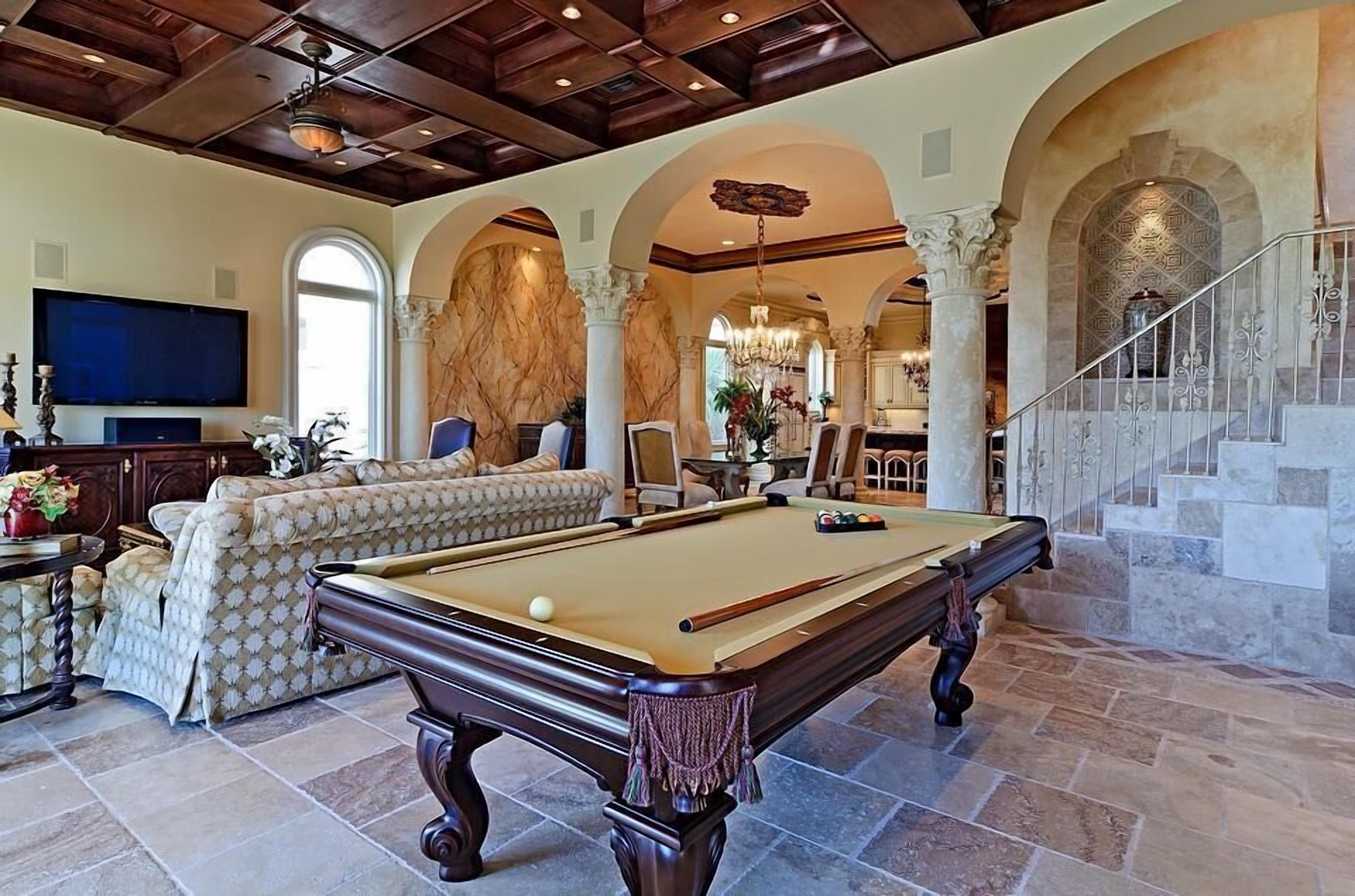 A spacious living room with a pool table, comfortable seating, and a staircase leading to an upper level.