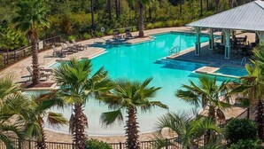 Ein großer Pool im Freien, umgeben von Palmen und Liegestühlen, mit einer überdachten Sitzgelegenheit im Hintergrund.