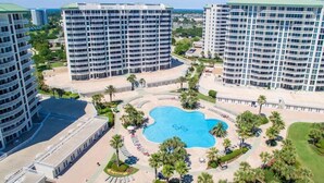 Ein Hochhotel mit einem zentral gelegenen Schwimmteich, umgeben von Palmen und Liegestühlen.