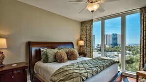 Ein Hotelzimmer mit einem großen Bett, einem Deckenventilator und Blick auf die Stadt durch große Fenster.