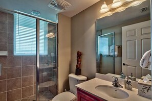 Een moderne badkamer met een douchecabine van glas, een wit toilet, een wastafel met spiegel en een grote wasbak.