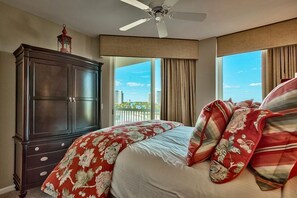 Een slaapkamer met een groot bed, een plafondventilator, een donker houten dressoir en uitzicht op de stad door grote ramen.
