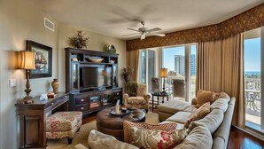 Ein geräumiges Wohnzimmer mit einer großen Couch, einem Fernseher und einem Balkon mit Blick auf die Stadt.