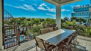 A covered outdoor area with a table and chairs, a pool, and a view of a building and palm trees.