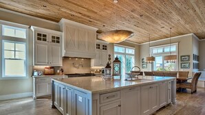 A spacious kitchen with a large island, white cabinetry, and a wooden ceiling.