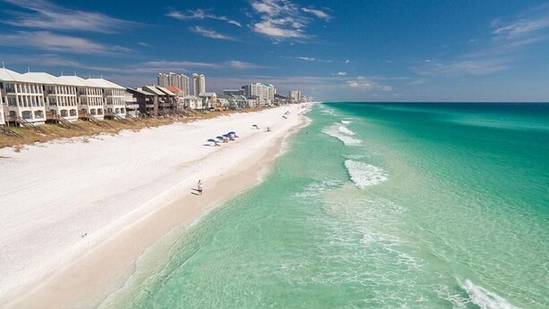 A beach with clear turquoise water, white sand, and a row of buildings along the shore.