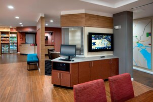 Un vestíbulo de hotel moderno con mostrador de recepción, zona de estar y una pantalla grande mostrando un evento deportivo.