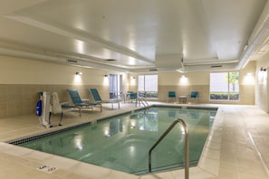 Una piscina con una silla de salvavidas, sillas de descanso y un ventanal con vistas al exterior.