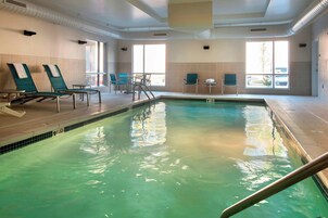 Una piscina interior con sillas y mesas de descanso, suelo de baldosas y ventanas amplias.