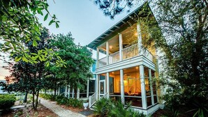 A two-story house with a balcony, surrounded by trees and a pathway. - Summer Dreams 4 Bedroom Holiday Home by Five Star Properties (Santa Rosa Beach)