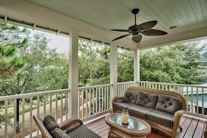 A covered porch with wicker furniture, a ceiling fan, and a view of trees.