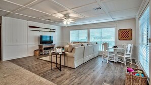 A spacious living room with a large sofa, a television, and a dining area with white chairs and a table.