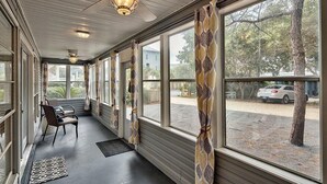 A covered porch with large windows, a ceiling fan, and a chair.