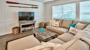 A living room with a television, wooden coffee table, beige sofa, and a window with blinds.