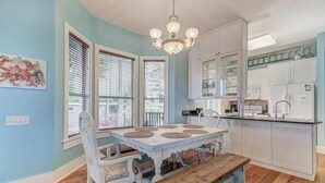 A dining area with a white table and bench, a chandelier, and a kitchen with white cabinets and a countertop. - GOING COASTAL 3 Bedroom Holiday Home by Five Star Properties (Panama City Beach)