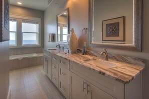 A modern bathroom with a large vanity, two sinks, a bathtub, and a large mirror.