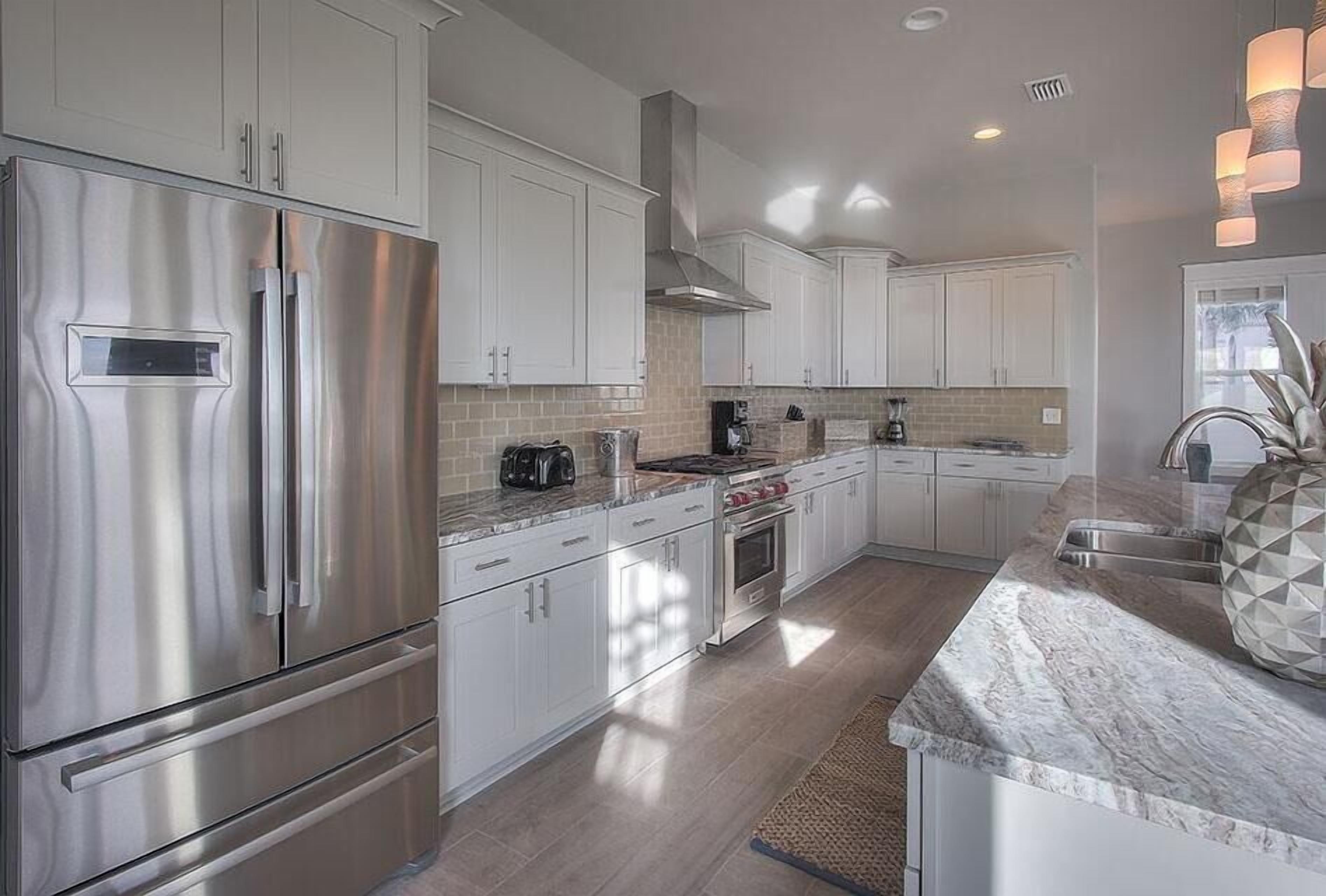 A modern kitchen with stainless steel appliances, white cabinetry, and a marble countertop.