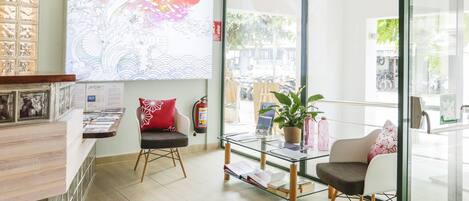 A reception area with a glass partition, a wooden reception desk, a fire extinguisher, a large floral artwork, and a view of the street outside.