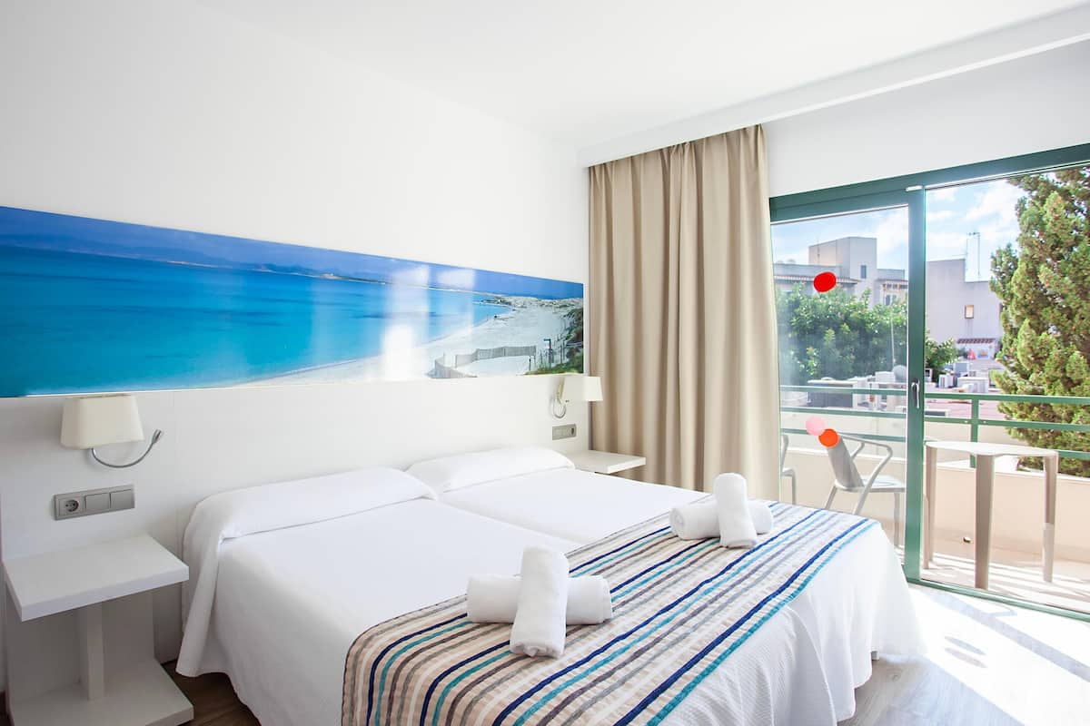 A hotel room with a bed, a nightstand, a lamp, and a view of the sea through a large window.
