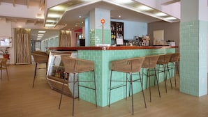 Un espace bar avec un comptoir recouvert de carreaux verts, des chaises en bois et une vitrine.