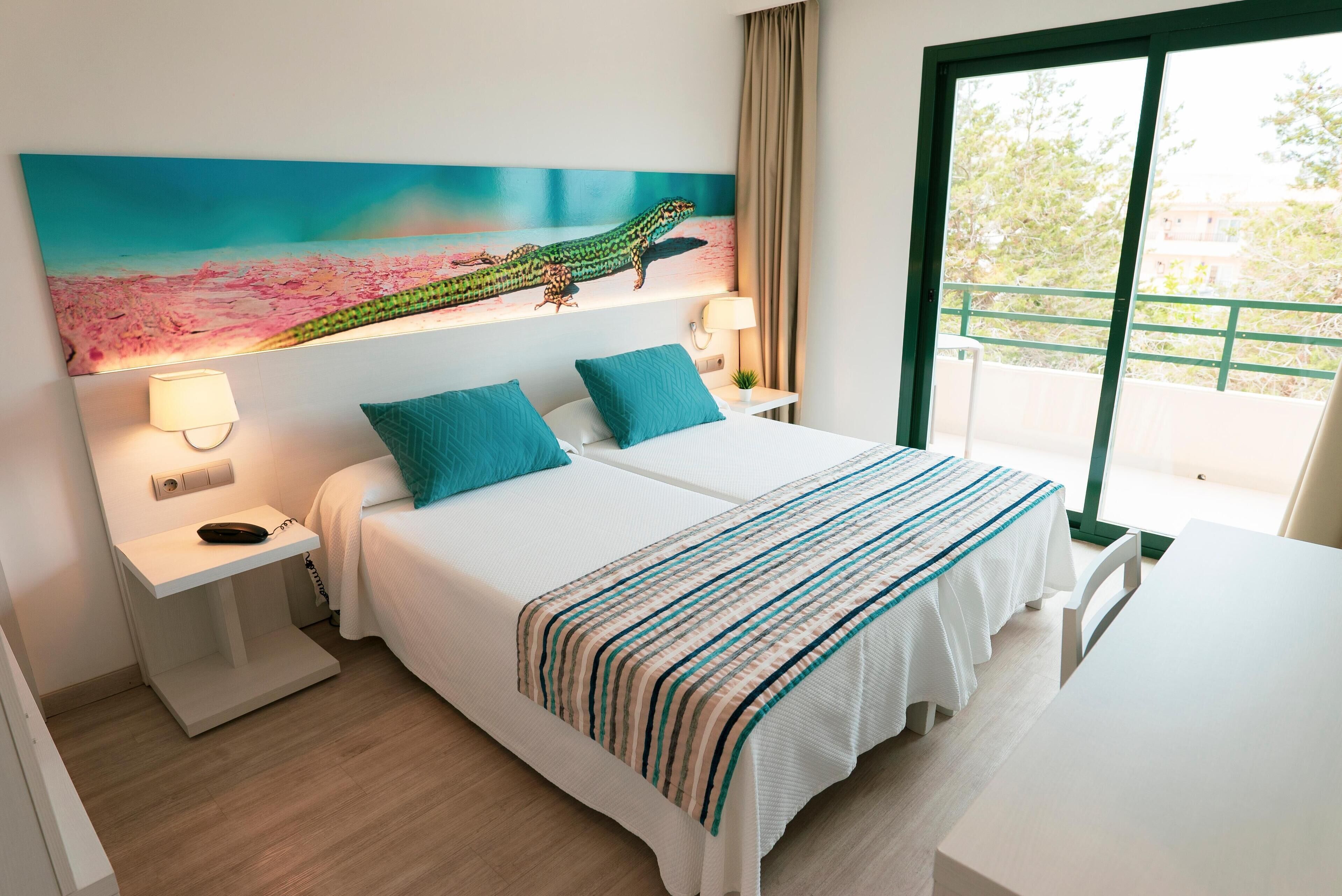 A hotel room with a bed, bedside tables, a desk, a chair, a painting on the wall, and a window with a view.