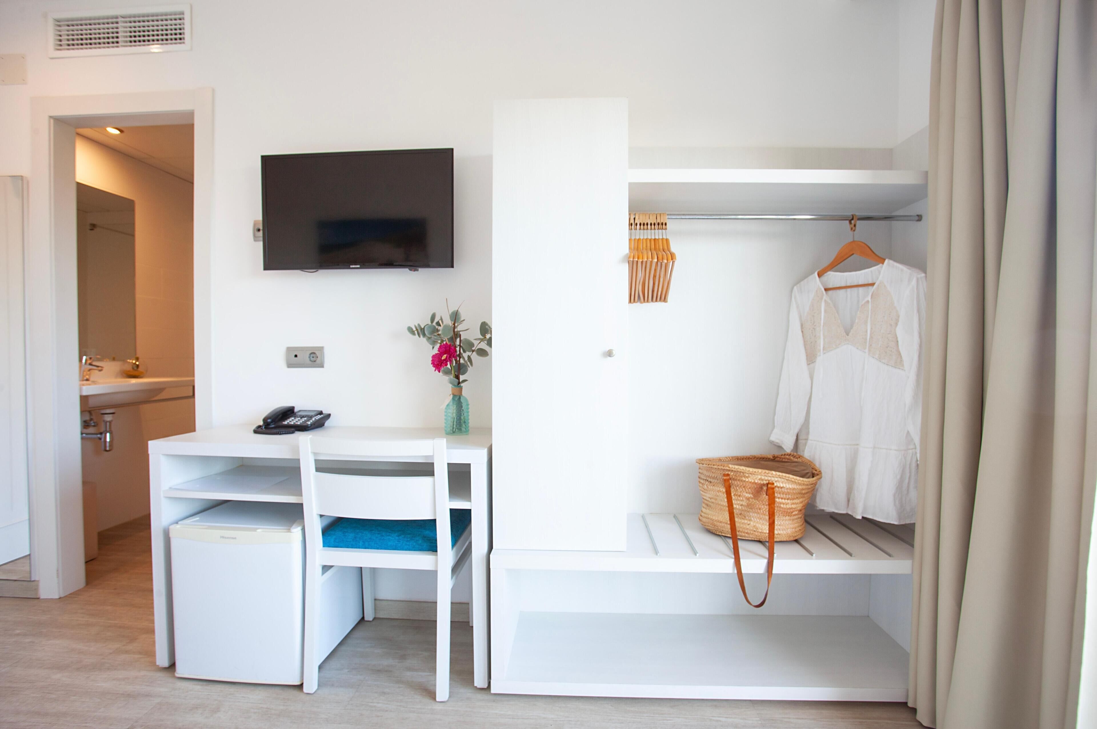 Habitación compacta con escritorio, televisión, baño pequeño y una cesta colgante.