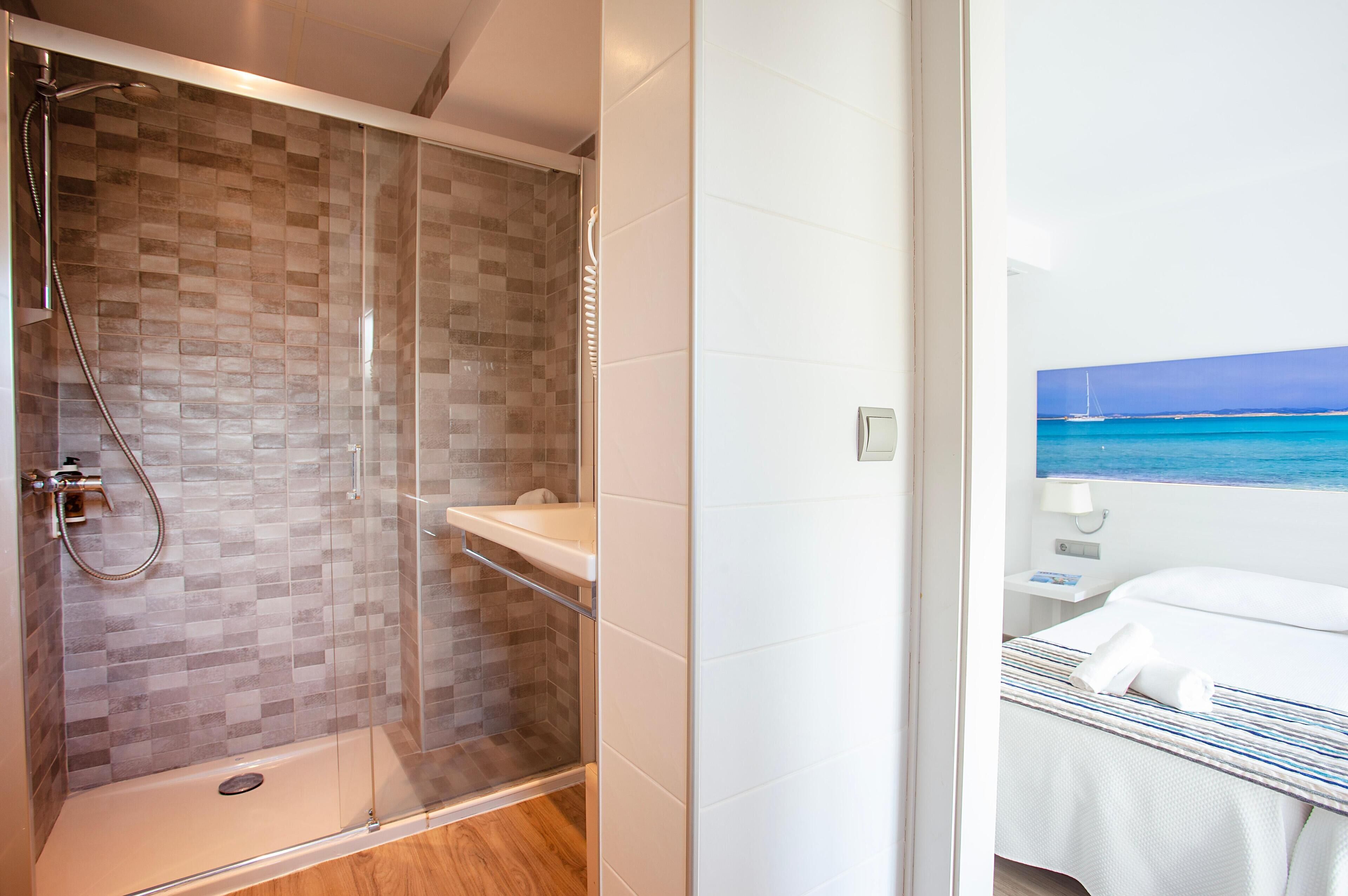A modern bathroom with a glass-enclosed shower, a white sink, and a view of the sea through a large window.
