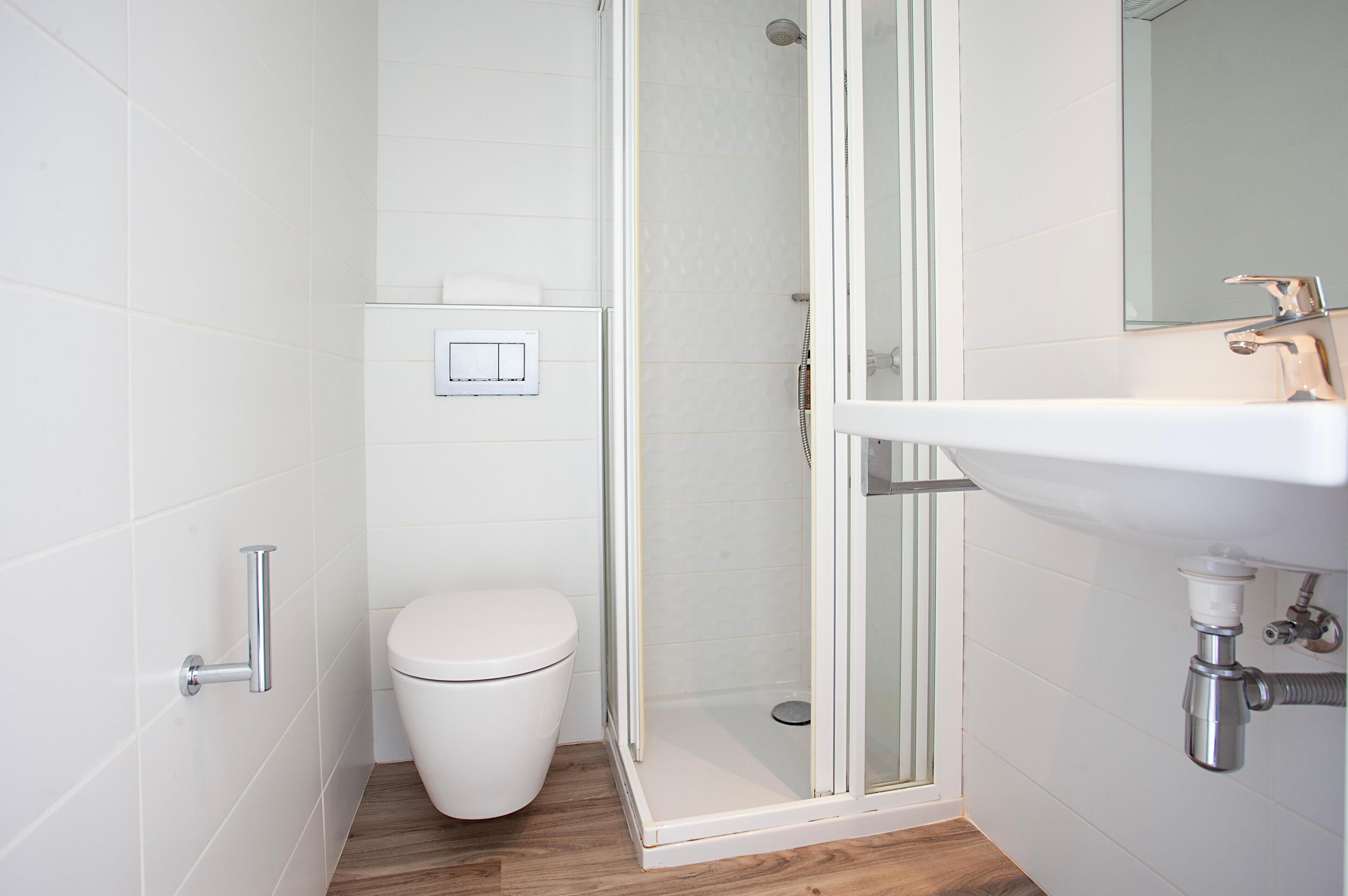 Un baño moderno con ducha envuelta en vidrio, inodoro blanco y lavabo con grifo cromado.